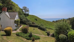 A white house with a sloped roof, surrounded by well-maintained gardens and a view of the sea. - Lynch Cottage (Lyme Regis)