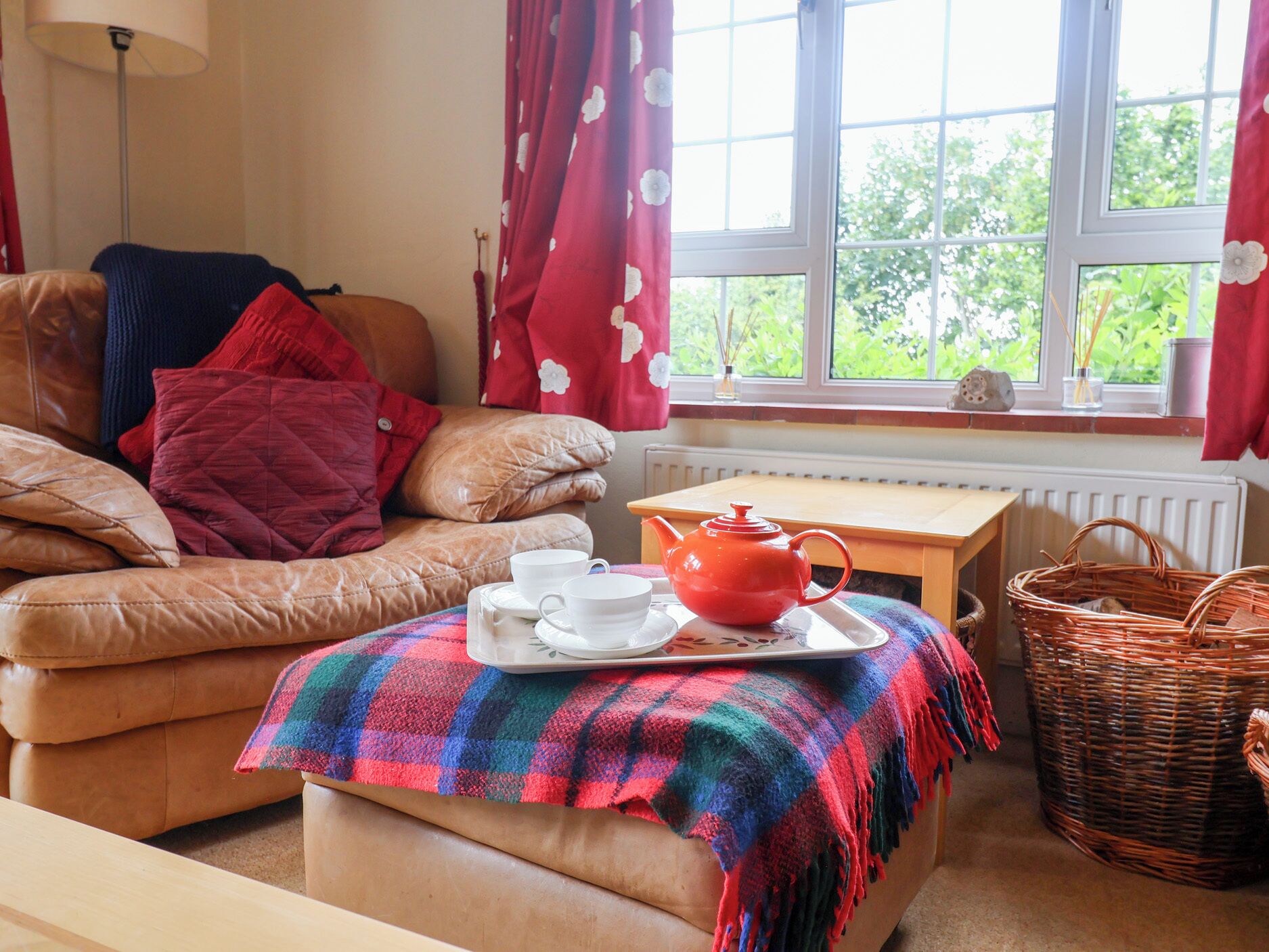 Een gezellige woonkamer met een leren bank, een geruite plaid, een rode theepot en een rieten mand.