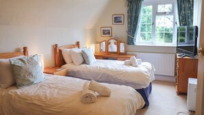 Een slaapkamer met twee bedden, een dressoir, een televisie en een raam met gordijnen.