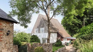 Een stenen huis met schuin dak, een geplaveid pad en een stenen muur met poort.