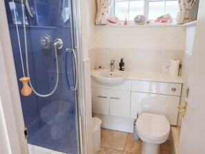A bathroom with a glass-enclosed shower, a sink, a toilet, and a window with curtains. - Barn Close Farm (Bridport)