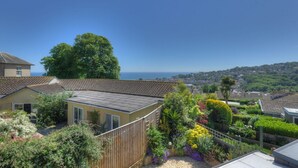 Área residencial com vista para o mar, com casas de telhado apaleira e diversas plantas e flores em primeiro plano.
