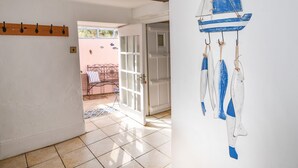 Um corredor com um cabideiro de madeira, um banco com almofada listrada e uma parede decorada com um veleiro azul.