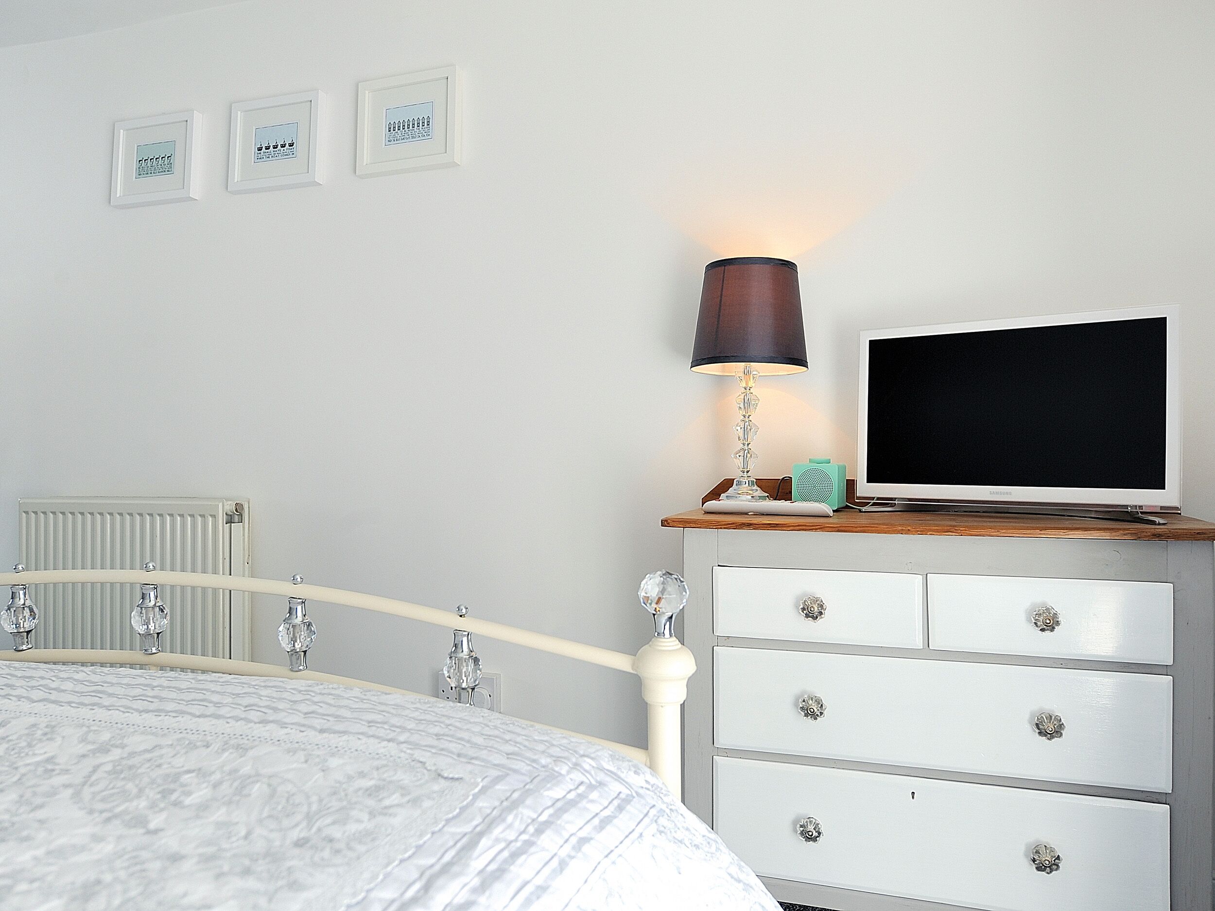 Et soveværelse med seng, et natbord med lampe, et fjernsyn og en kommode.