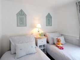 Un dormitorio con dos camas, cada una con ropa de cama y almohadas a rayas. Hay adornos en la pared sobre las camas y una mesita de noche con una lámpara y una caja de pañuelos.