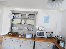 Una cocina con encimera de madera, microondas, cafetera y repisas con diversos utensilios de cocina.