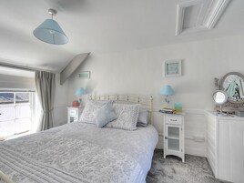 Un dormitorio con cama, mesitas de noche, cómoda, espejo y ventana con cortinas.