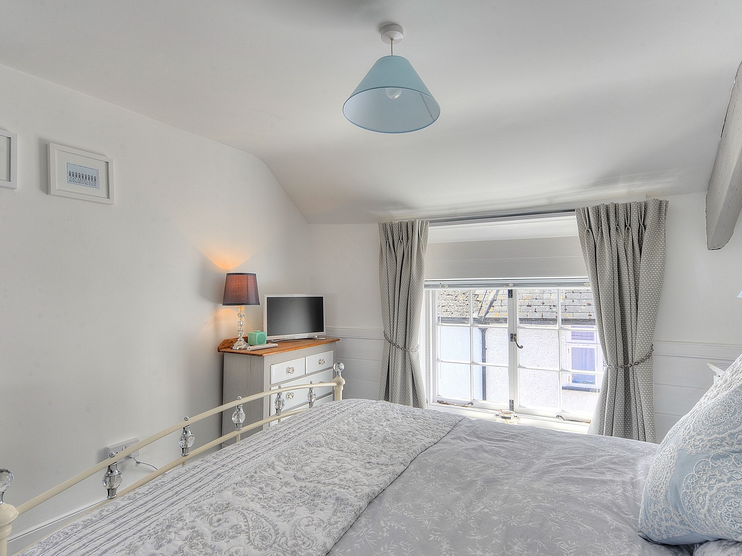 Ein Schlafzimmer mit einem Bett, einem Nachttisch mit Lampe, einem Fernseher und einem Fenster mit Vorhängen.