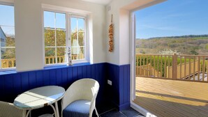 A balcony with a view of a forested landscape, a white wicker chair, and a small table. - Hillside Cottage (Lyme Regis)
