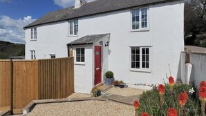 A white two-story house with a red door, windows, and a wooden fence. - Hillside Cottage (Lyme Regis)