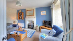 A cozy living room with a sofa, a blue armchair, a fireplace, and a television. - Hillside Cottage (Lyme Regis)
