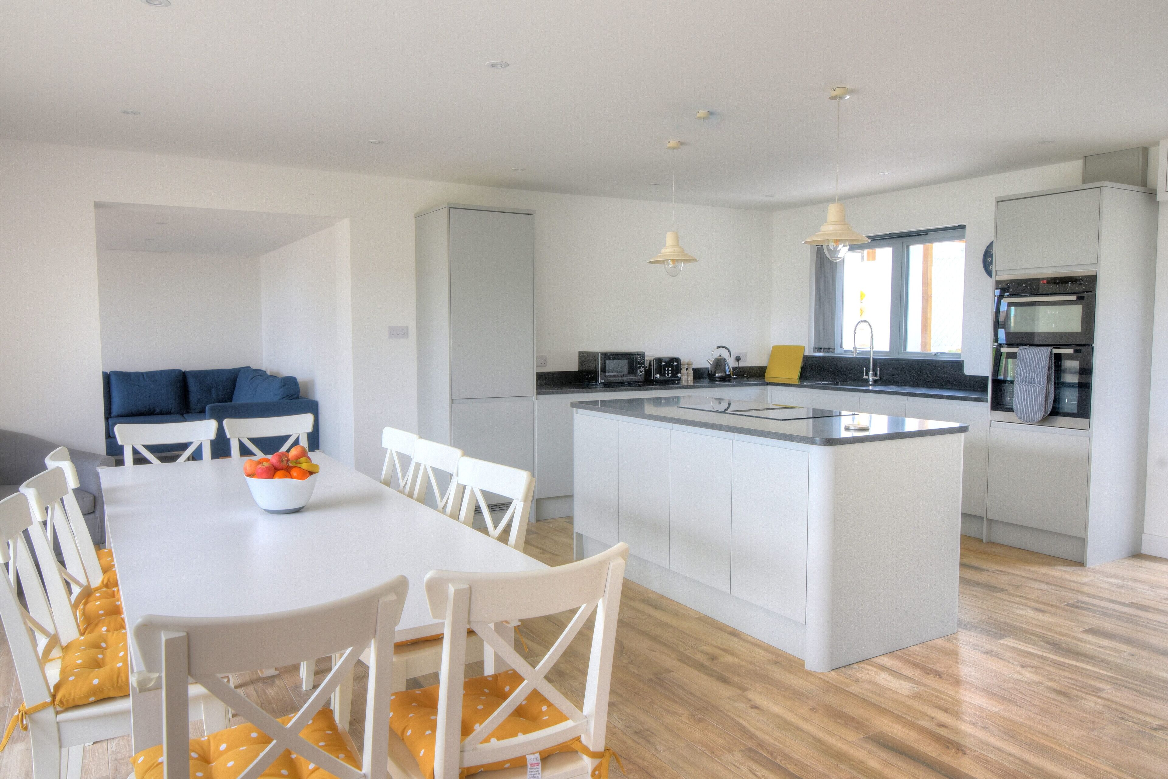 A modern kitchen with white cabinetry, a central island, and a dining area with white chairs and a table.