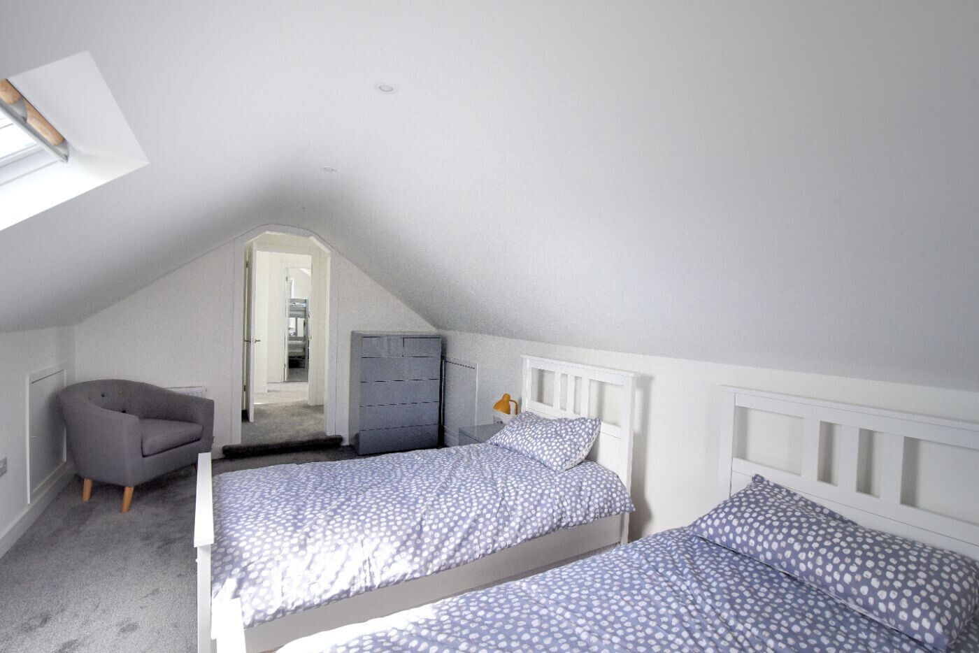 Une chambre avec deux lits, une chaise, une commode et une lucarne.