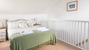 Ein Schlafzimmer mit einem Bett, zwei Nachttischen, einer grünen Tagesdecke, einem weißen Geländer und einem gerahmten Bild an der Wand.