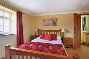 Un dormitorio con cama de madera, ropa de cama roja, dos mesitas de noche con lámparas, una ventana con cortinas rojas y una puerta de madera.