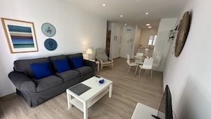 A modern living room with a grey sofa, a coffee table, and a dining area with white chairs and a glass table. - Nerja Paradise Rentals - Apartment El Califa 3 (Nerja)