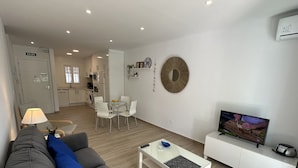 A modern living room with a sofa, a coffee table, a TV, and a dining area with chairs. - Nerja Paradise Rentals - Apartment El Califa 3 (Nerja)