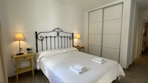 A hotel room with a bed, two bedside tables with lamps, a large wardrobe, and a wooden floor. - Nerja Paradise Rentals - Apartment El Califa 3 (Nerja)