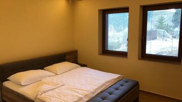A bedroom with a large bed, two windows, and a wooden headboard.