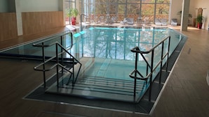 A large indoor swimming pool with glass walls, surrounded by lounge chairs and a view of trees through large windows. - Villa Golf (Karlovy Vary)