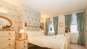A bedroom with a four-poster bed, a dresser, a mirror, and a window with curtains.