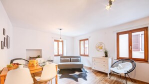 Een moderne kamer met een bed, een eettafel met stoelen, een vachttapijt van koeienleer, een zwarte stoel en een dressoir.