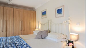 A bedroom with a bed, wooden wardrobe, two framed pictures on the wall, a bedside lamp, and a book on the nightstand. - 1 Woodroffe Meadow (Lyme Regis)