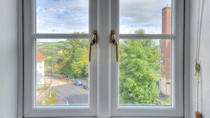 A window with a white frame and two brass handles, offering a view of a green landscape with trees and a road. - 1 Woodroffe Meadow (Lyme Regis)