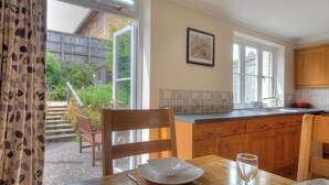 A kitchen with wooden cabinets, a tiled backsplash, and a window overlooking a garden. - 1 Woodroffe Meadow (Lyme Regis)
