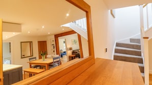 Un intérieur moderne avec une table à manger en bois, un escalier et un grand miroir qui reflète la pièce.