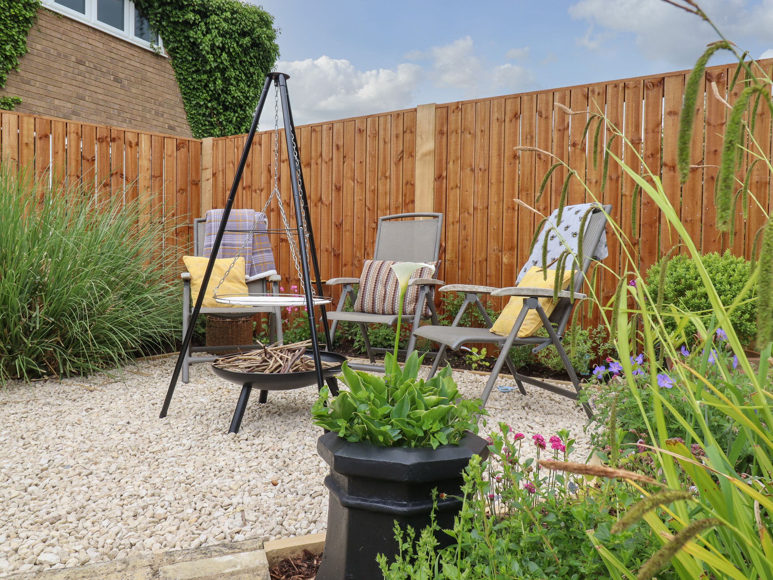 A patio with two chairs, a hanging swing, and a planter with green plants.