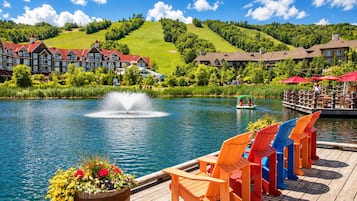 Ein Seehotel mit Steg, bunten Adirondack-Stühlen, einer Fontäne und einem Boot.
