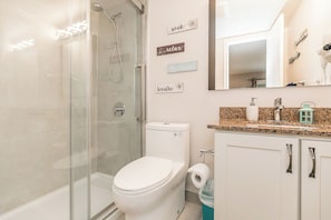 A bathroom with a glass-enclosed shower, a toilet, a sink with a mirror, and wall-mounted signs with motivational phrases. - Newly Renovated Ski-In Studio: Hot Tubs, Pool, Tennis, Walk or Ski to Slopes (Blue Mountains)
