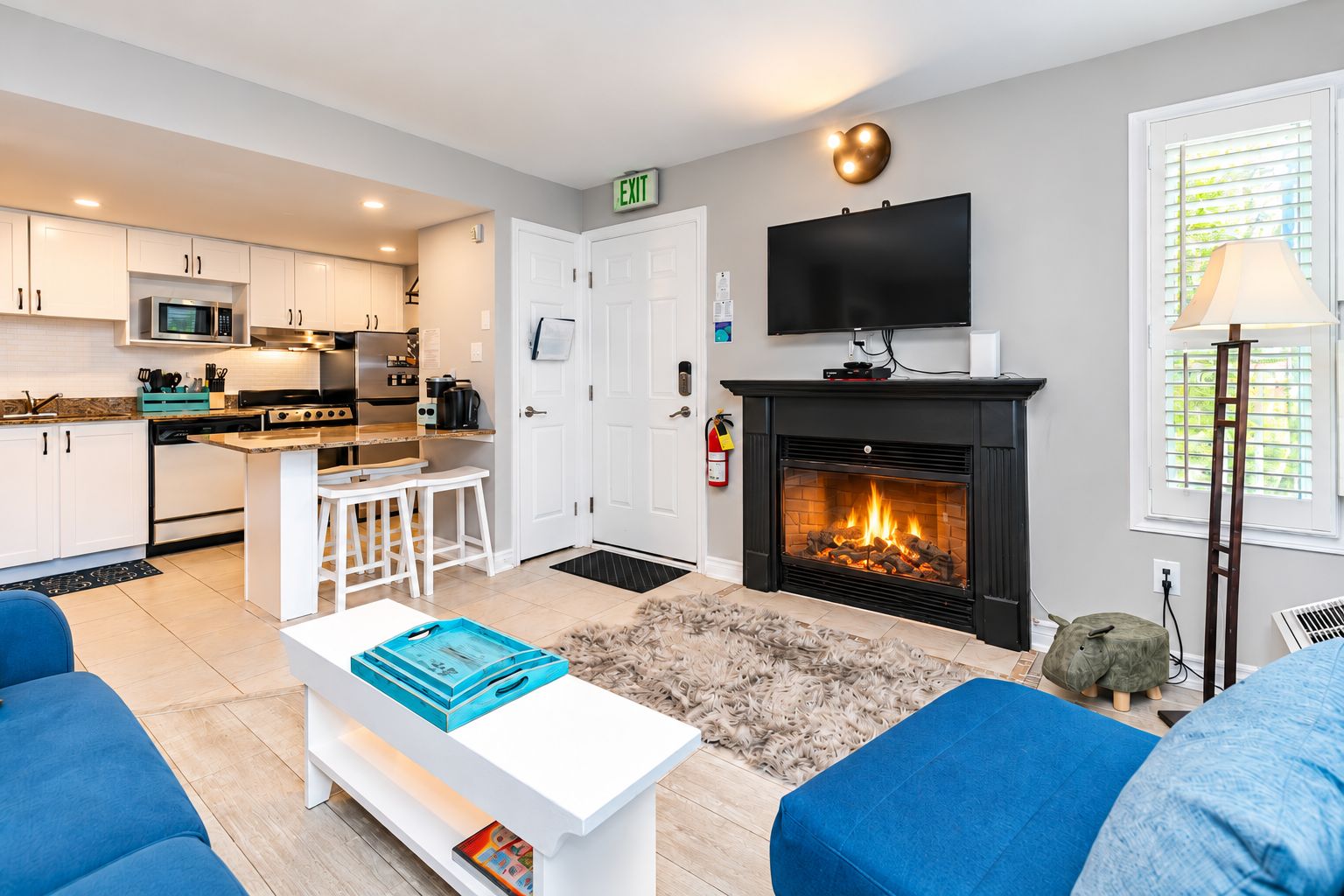 Ein modernes Wohnzimmer mit Kamin, Fernseher und einer Küche im Hintergrund.