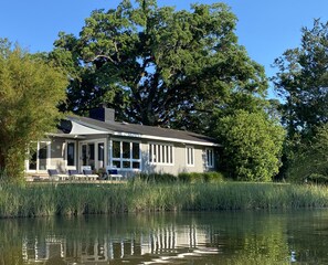 Uma casa à beira de um lago, com varanda coberta e grandes janelas.