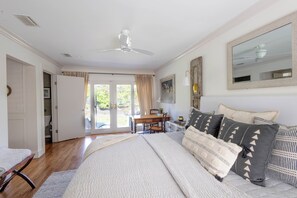 Une chambre à coucher comprenant un lit, un bureau, une chaise, un ventilateur de plafond et un grand miroir.