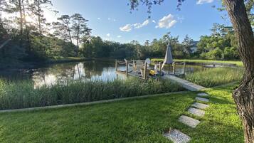 Un parque tranquilo junto al lago, con un muelle de madera, sillas y una mesa de picnic.