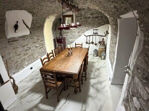 Un coin repas avec une table et des chaises en bois, des murs en pierre et des ustensiles de cuisine suspendus.