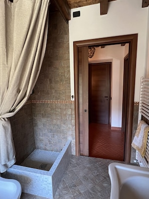 A bathroom with a shower, tiled walls, a wooden door, and a towel rack.
