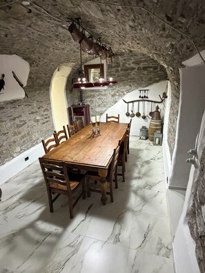 A dining area with a wooden table and chairs, a stone wall, and a hanging light fixture. - Casa Boru - a beautiful fully restored spacious house with fantastic views (Calice al Cornoviglio)