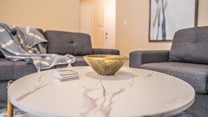 Un saló modern amb una taula de centre rodona de marbre, un sofà gris i un bol decoratiu.