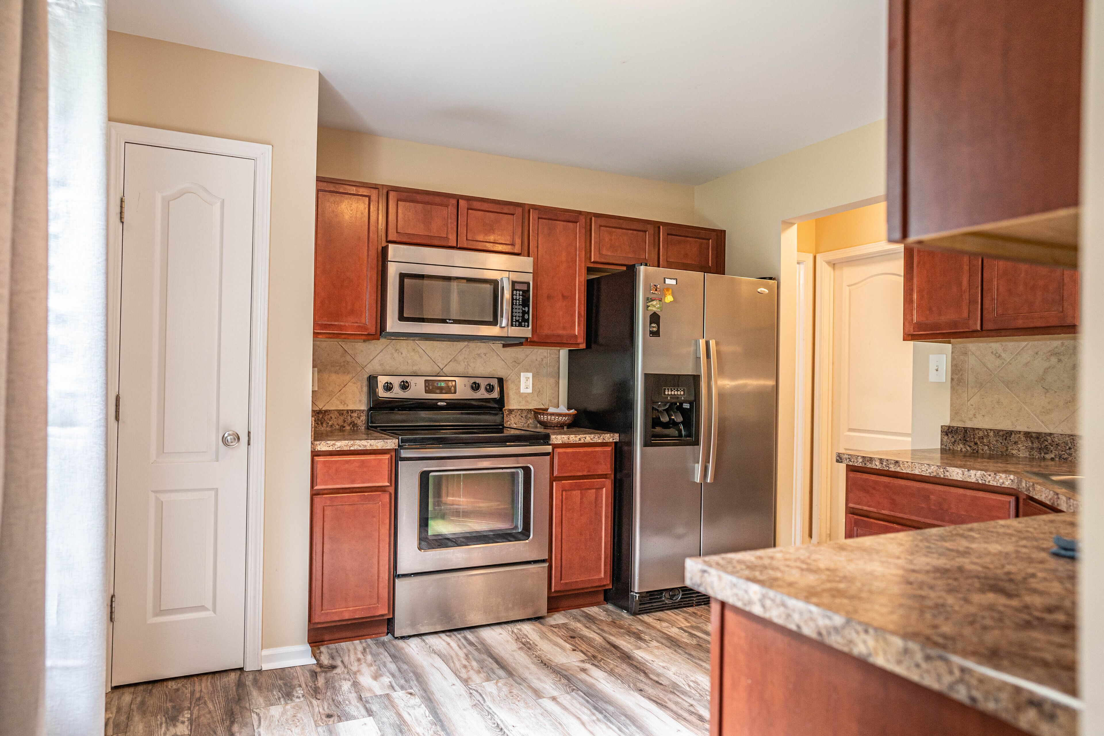 A kitchen with wooden cabinets, a stainless steel refrigerator, a microwave, an oven, and granite countertops.