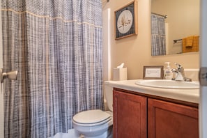 A bathroom with a plaid shower curtain, a toilet, a sink with a soap dispenser, and a framed sign on the wall. - Putt in the Pines 3BD 2 BA Charming Quiet Home (Aberdeen)