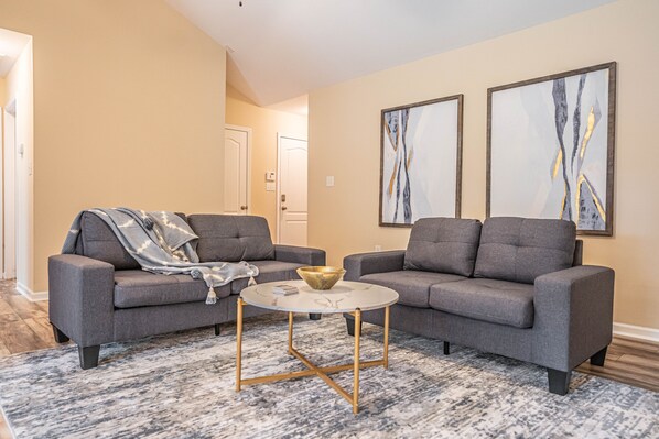 A living room with two grey sofas, a round coffee table with a bowl, and abstract paintings on the wall. - Putt in the Pines 3BD 2 BA Charming Quiet Home (Aberdeen)