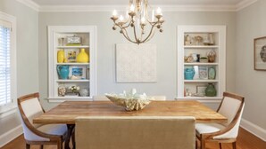 A dining room with a wooden table, white chairs, and a chandelier. There are two white shelves with decorative items and a framed artwork above the table. - Beautiful Bright 6 bedroom home in the heart of Buckhead (Atlanta)