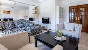 A living room with a patterned sofa, a white sofa, a black coffee table, and a television. - Cantinho da fraternidade - 3 bed apartment (Portimão)