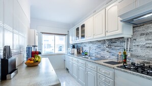 A modern kitchen with white cabinets, a granite countertop, a gas stove, and a window providing natural light. - Cantinho da fraternidade - 3 bed apartment (Portimão)
