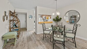 Un coin repas avec une table ronde et des chaises, un escalier en bois et une cuisine en arrière-plan.