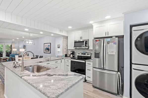 A modern kitchen with stainless steel appliances, a granite countertop, and white cabinetry.