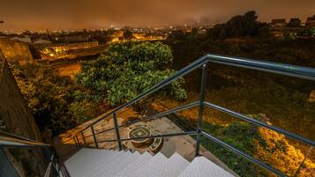A staircase with metal railings leading to a higher level, surrounded by greenery and a cityscape at night.